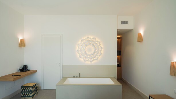 Un baño moderno con una bañera independiente, un tocador de madera, una lámpara de pared decorativa y una mesita de noche pequeña.
