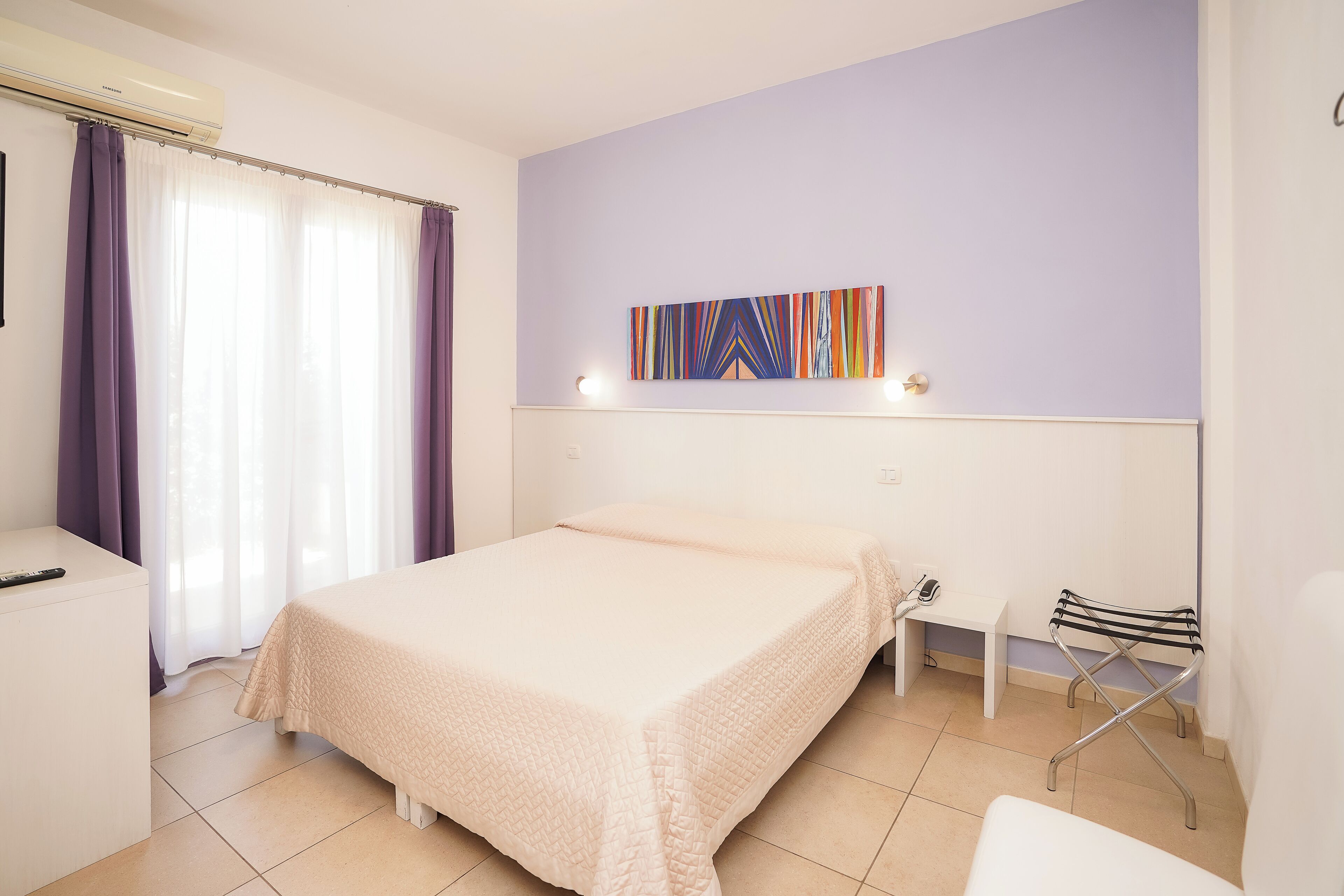 Habitación de hotel con cama, escritorio, silla, una mesita y una obra de arte en la pared.