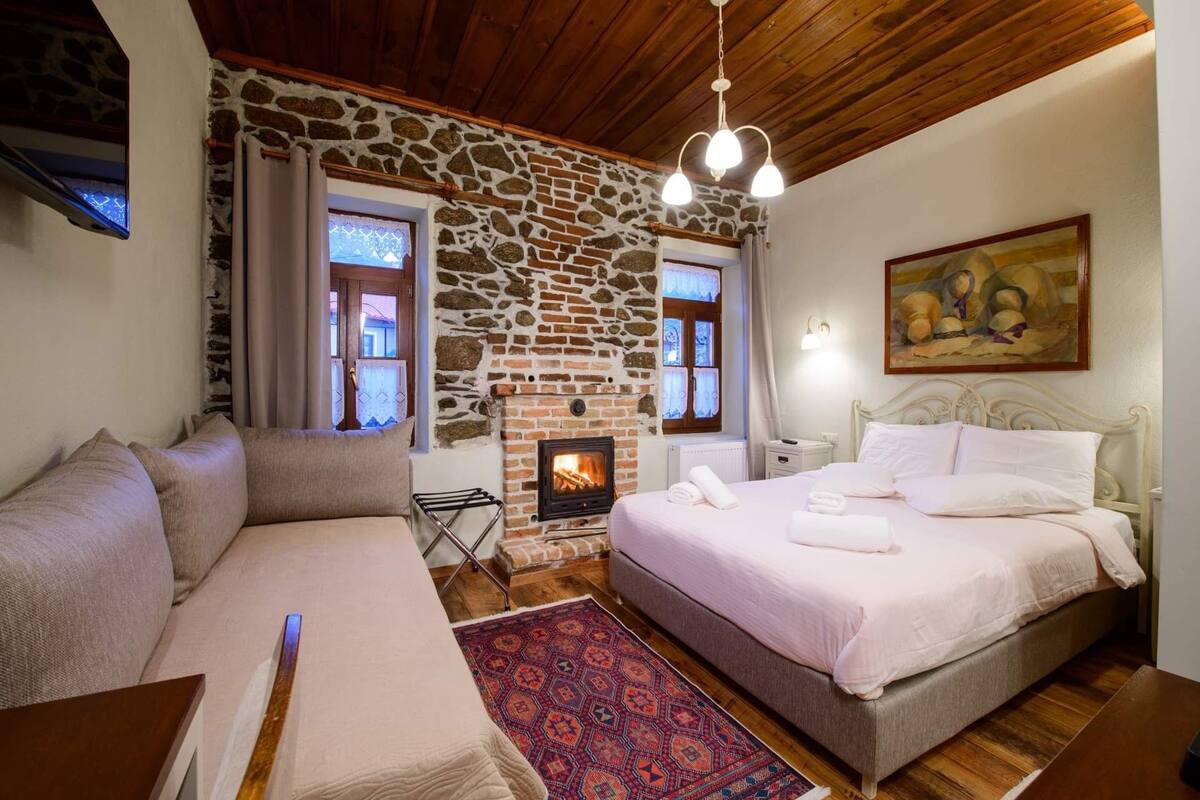Un dormitorio acogedor con pared de piedra, chimenea, cama con almohadas, sofá y alfombra.