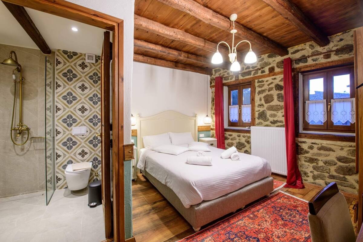 Un dormitorio con cama, ventana con cortinas, ducha y pared de piedra.