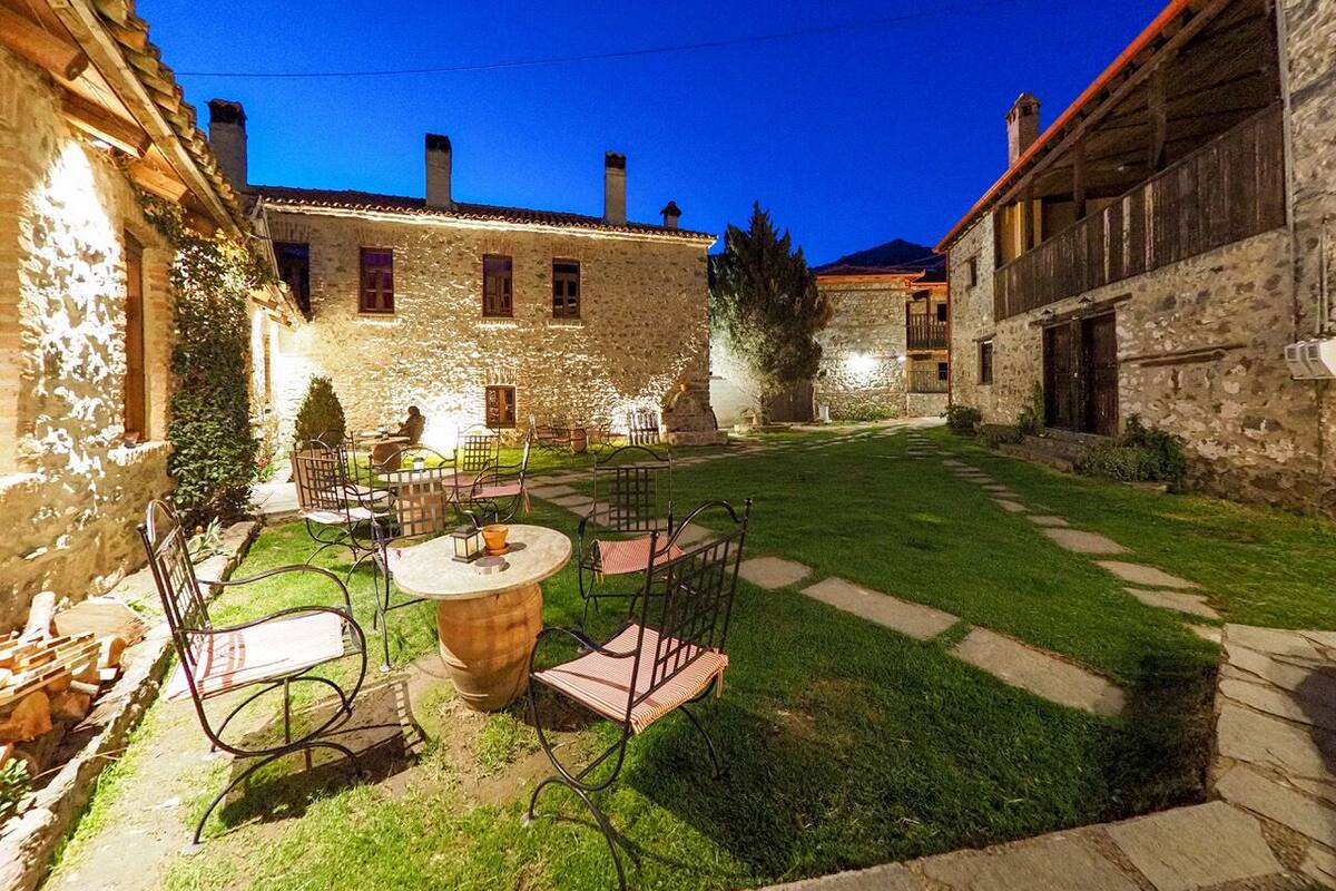 Un patio con edificios de piedra, un sendero empedrado y mobiliario exterior con sillas y una mesa.