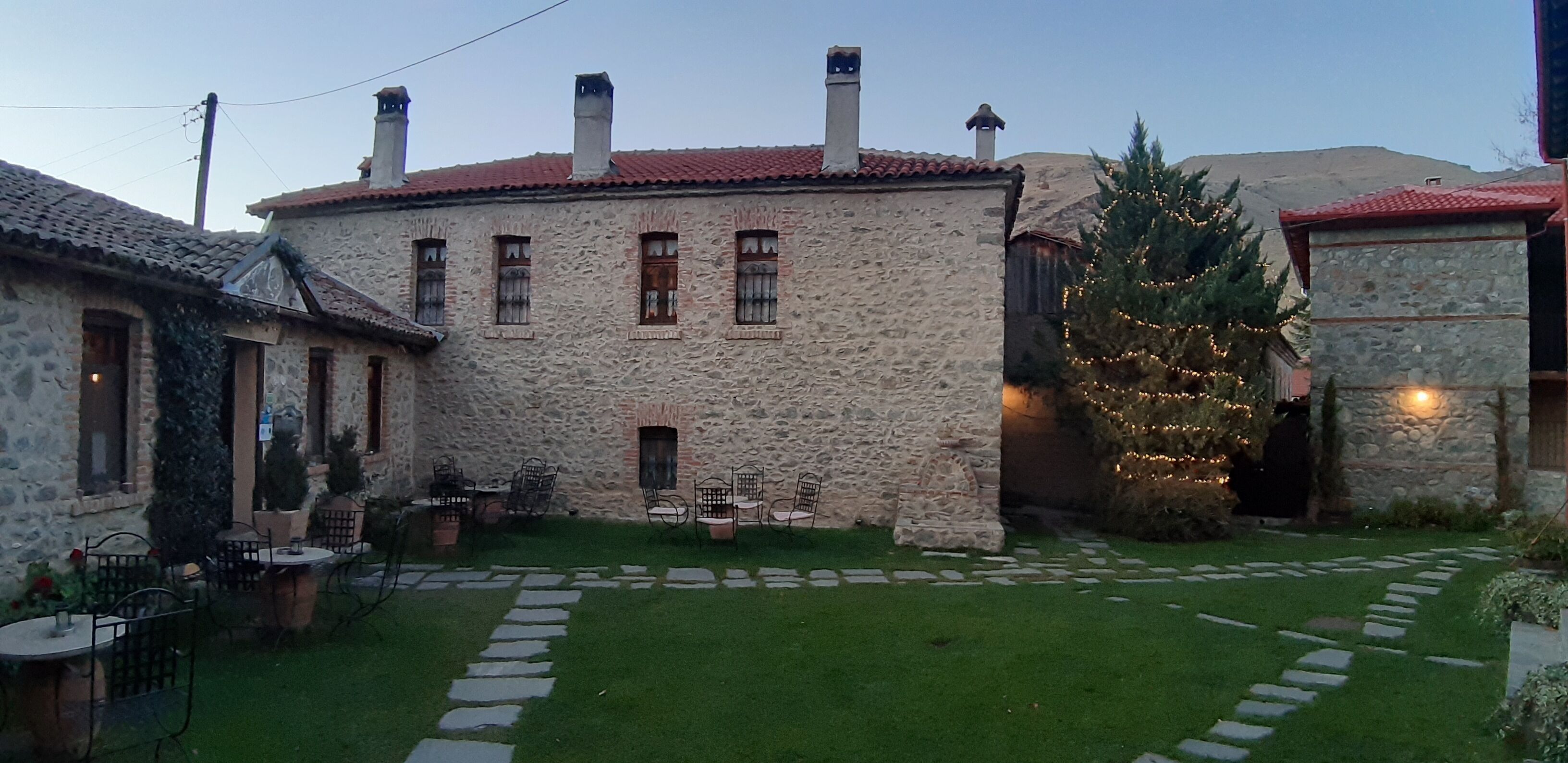 A stone building with a red-tiled roof, a small garden with a Christmas tree, and outdoor seating.