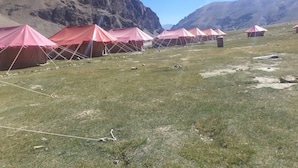 A row of red tents in a grassy field with mountains in the background. - Himalayan Routes Camp (Lahul)