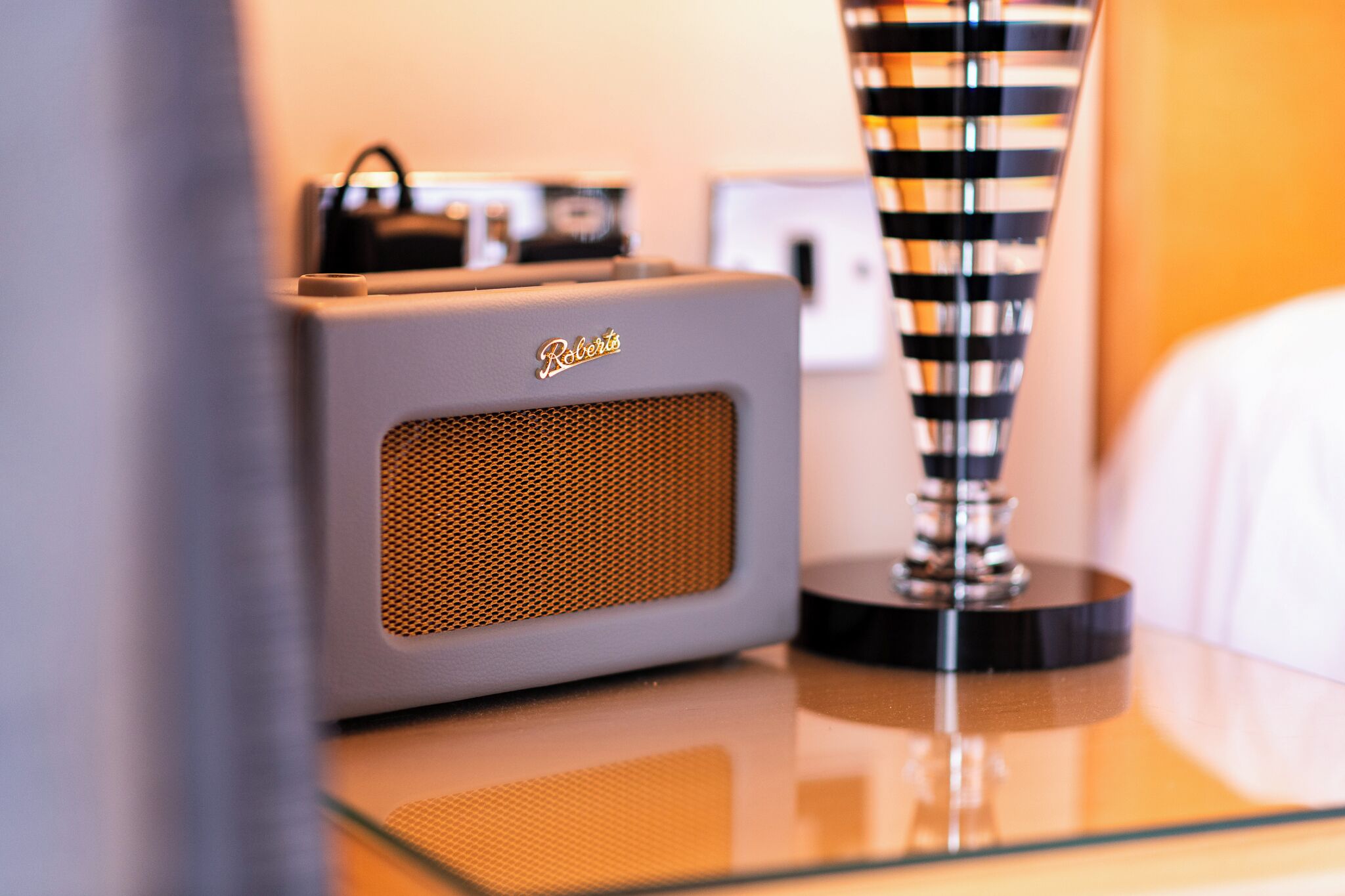 Un altavoz con frente de malla y un logotipo, un florero a rayas y un sofá blanco.