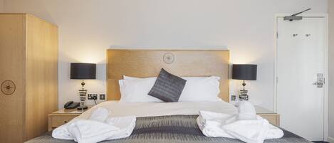 A neatly made bed with white linens, two bedside lamps, and a wooden headboard.