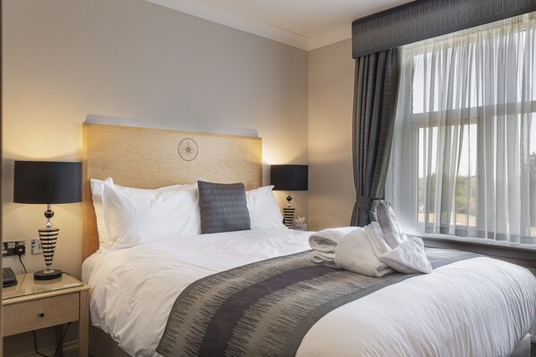 A hotel room with a neatly made bed, two bedside lamps, a nightstand with a lamp, a window with curtains, and a view of the outdoors. - The Moorland Hotel, Haytor, Devon (Newton Abbot)
