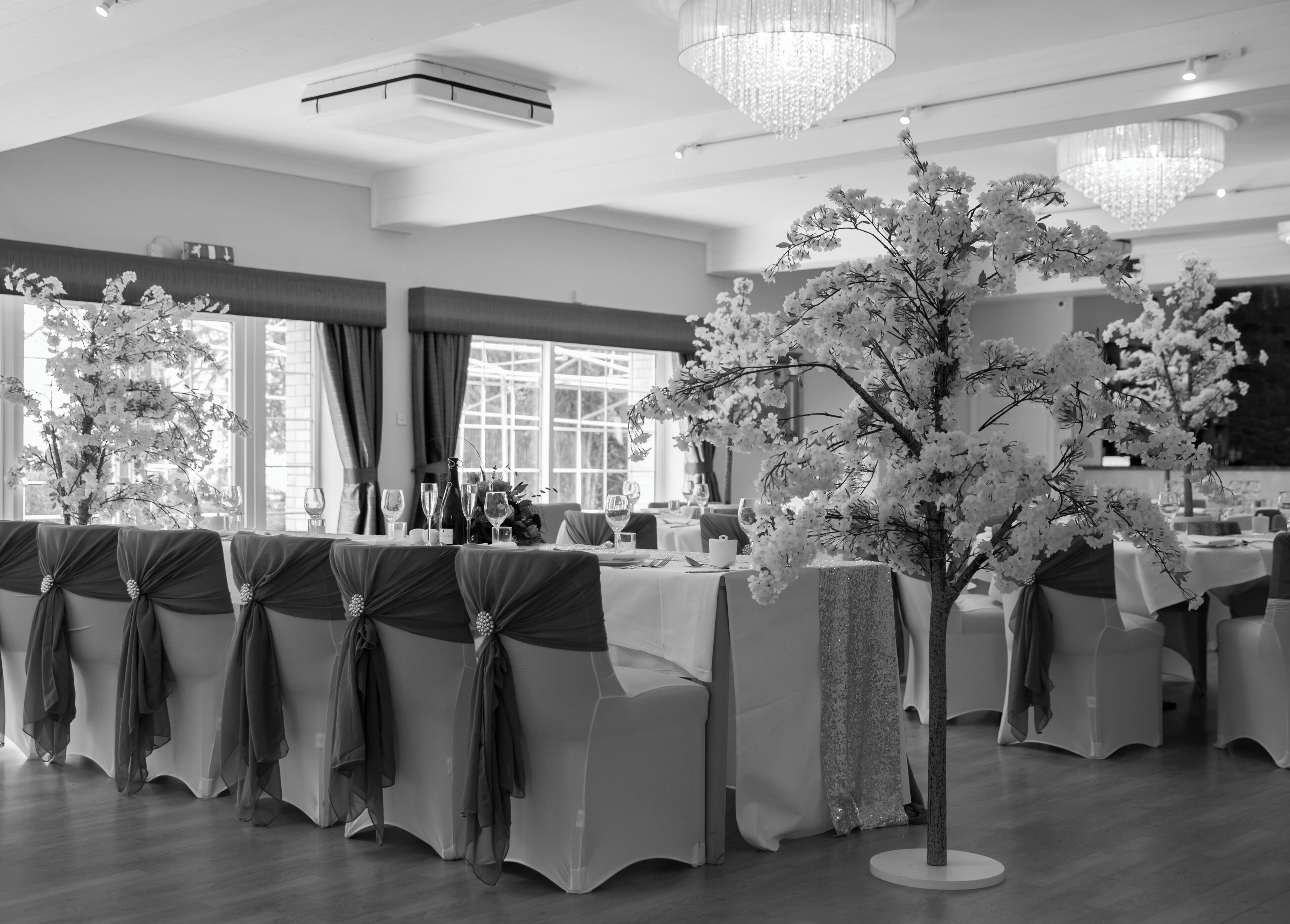 Ein Festsaal mit gedeckten Tischen für eine festliche Veranstaltung, mit Kristalllüstern und floralen Tischdekorationen.