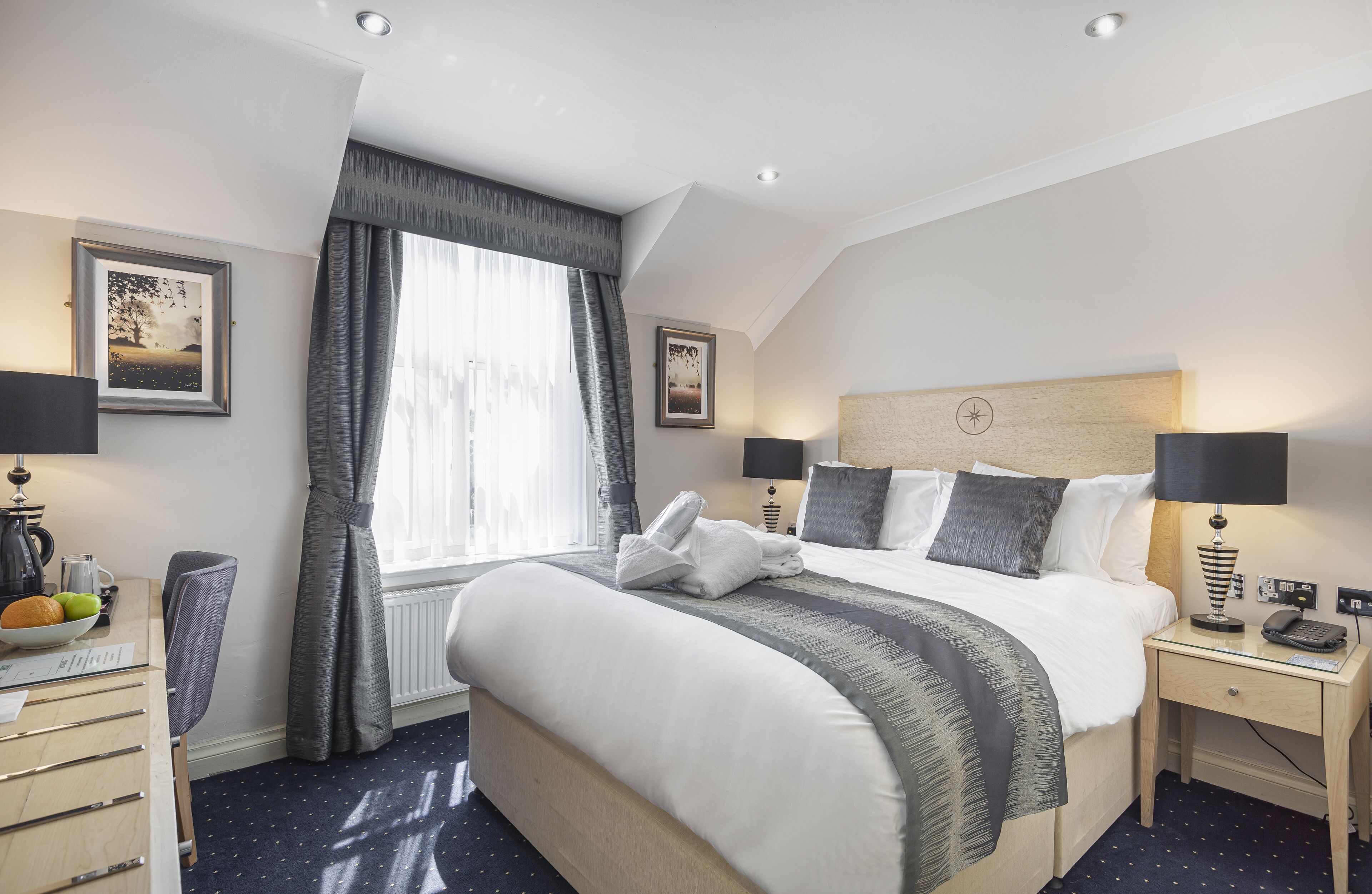 Une chambre d’hôtel avec un grand lit, deux tables de chevet avec des lampes, un bureau avec une chaise et une fenêtre avec des rideaux.