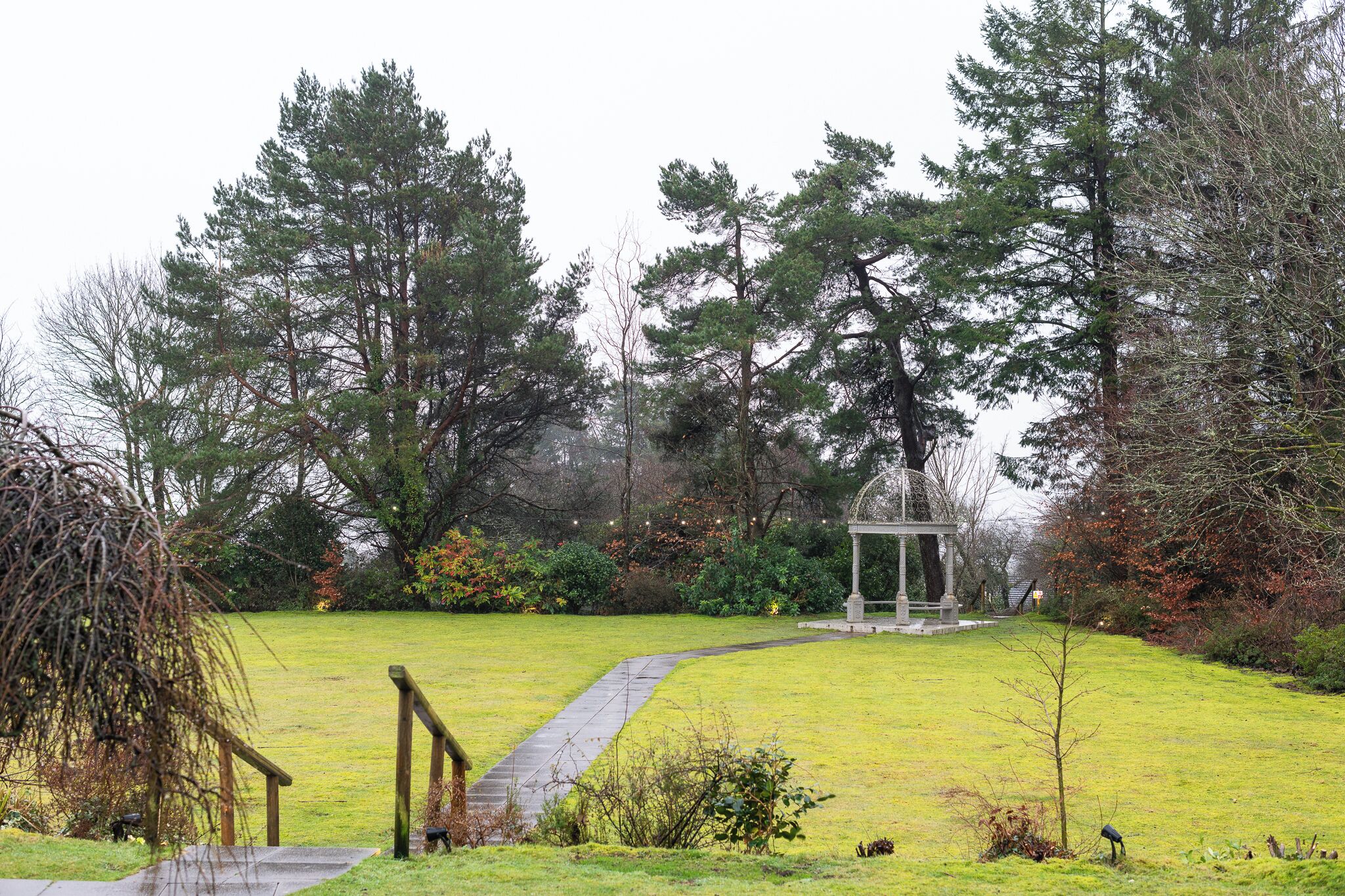 Um jardim com um gazebo, um caminho e árvores altas.