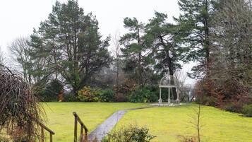 Um jardim com um gazebo, um caminho e árvores altas.