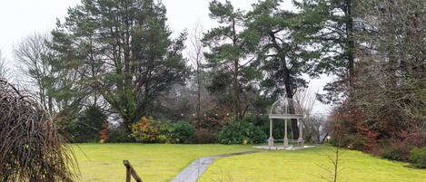 A garden with a gazebo, a pathway, and tall trees.