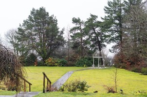 Um jardim com um gazebo, um caminho e árvores altas.