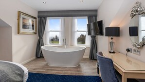 Une salle de bain moderne avec une baignoire sur pieds, un meuble-lavabo avec un miroir et un téléviseur fixé au mur.