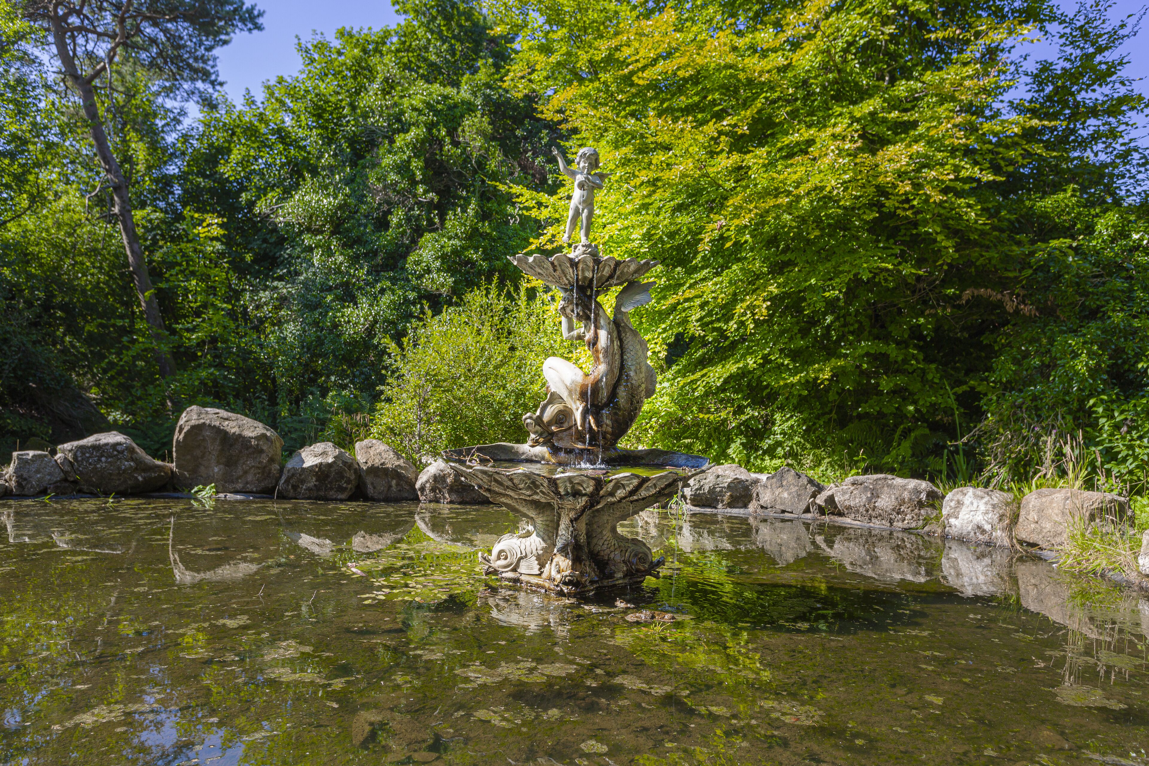 A fountain with a statue of a child and a bird, surrounded by rocks and greenery.