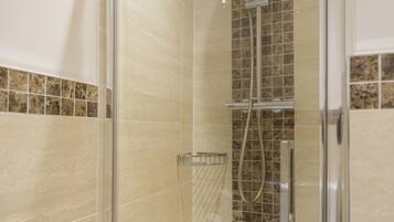 A glass-enclosed shower with a vertical tile backsplash and a handheld showerhead.