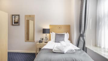 A hotel room with a neatly made bed, a bedside table with a lamp, a mirror, and a window with curtains.