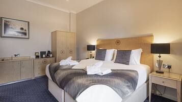 A hotel room with a large bed, two bedside tables with lamps, a wardrobe, a desk with a coffee maker, and a framed picture on the wall.