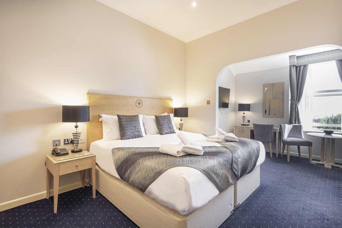 Een hotelkamer met een groot bed, nachtkastjes met lampen, een bureau en een stoel.