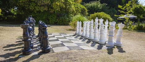 A large outdoor chessboard set up on a grassy field with trees in the background.