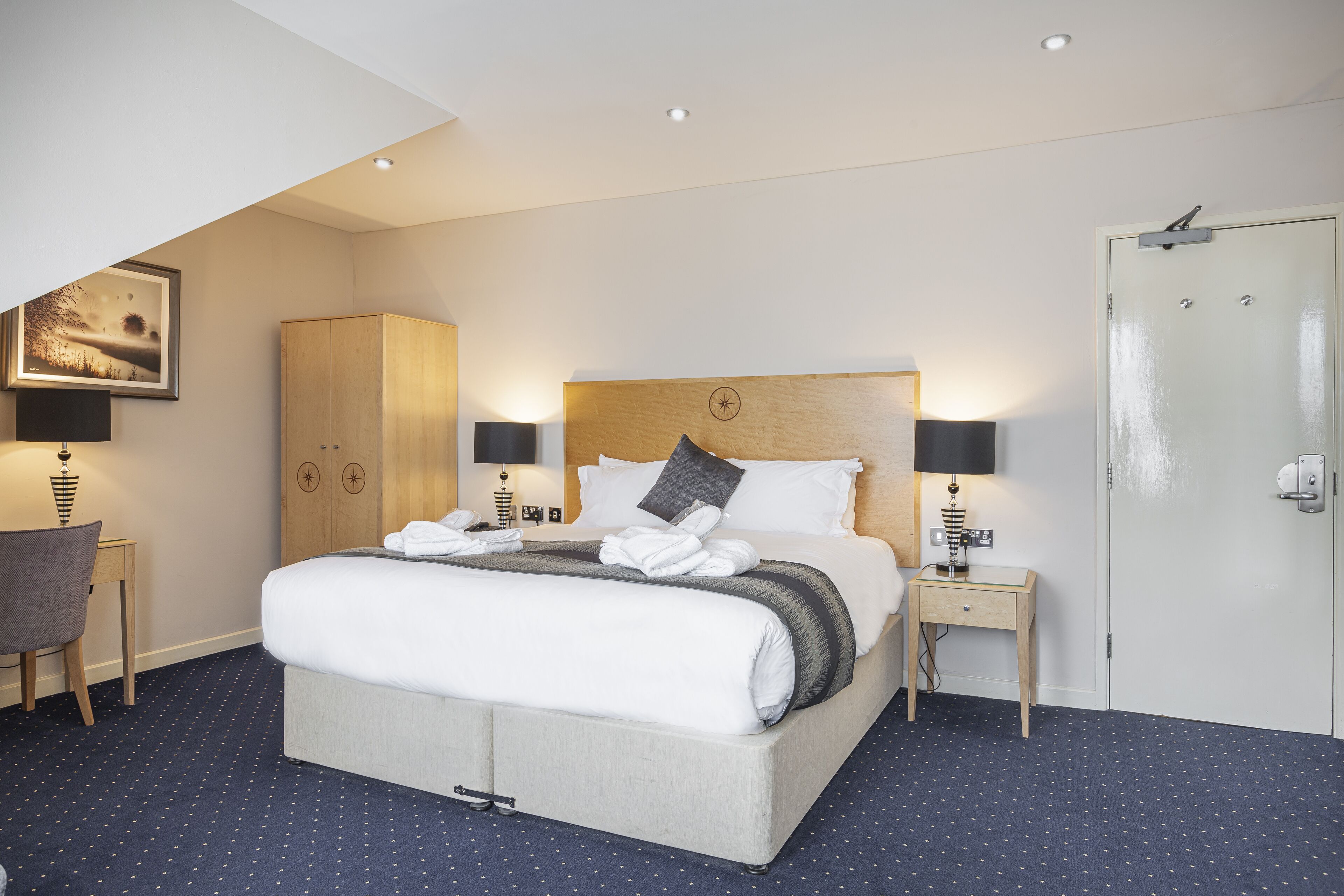 A hotel room with a large bed, two bedside tables, a wardrobe, and a door.