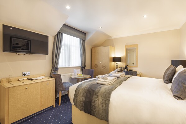Habitación de hotel con cama, escritorio, silla, armario, televisor y ventana con cortinas.