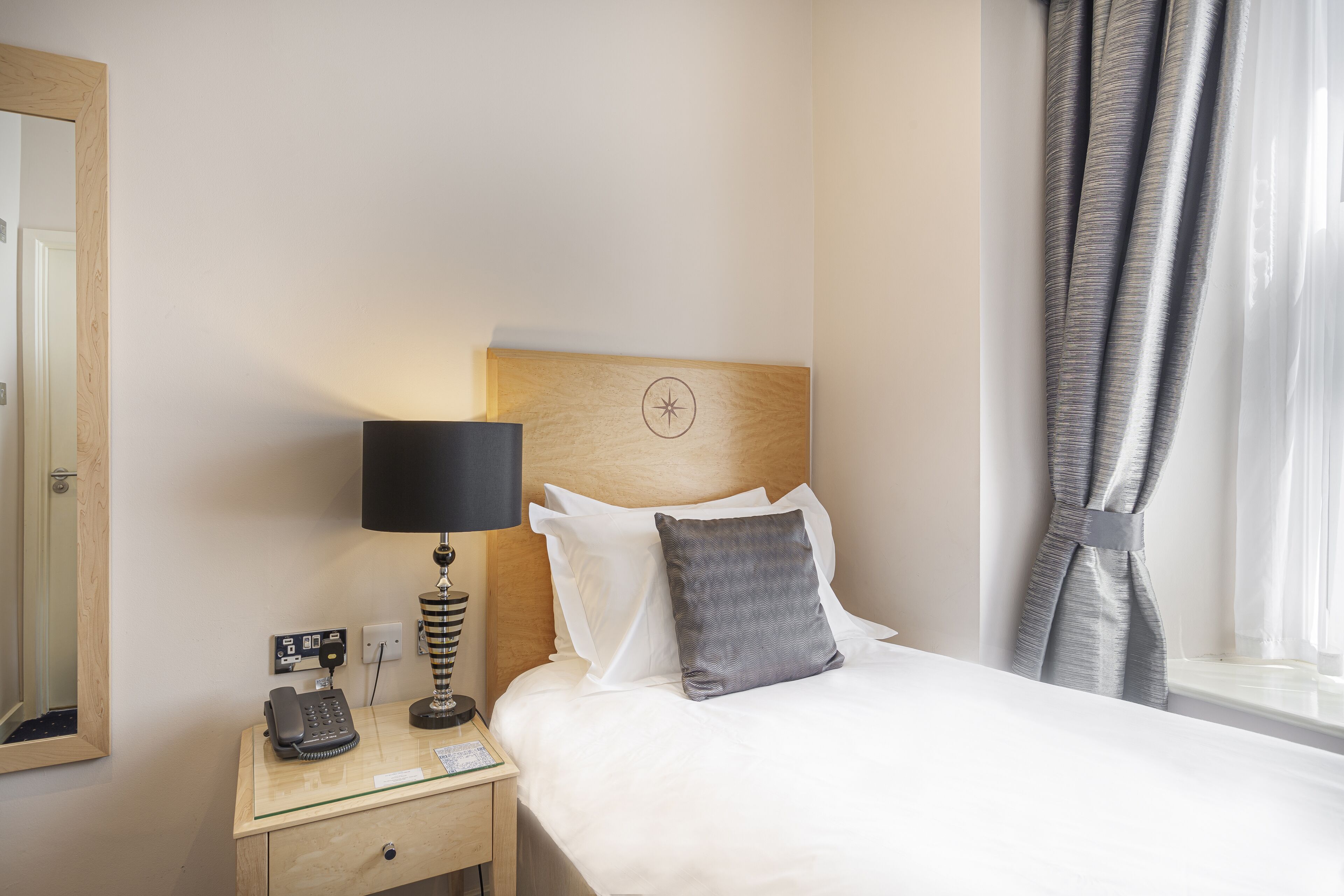 A hotel room with a bed, a bedside lamp, a telephone, and a window with curtains.