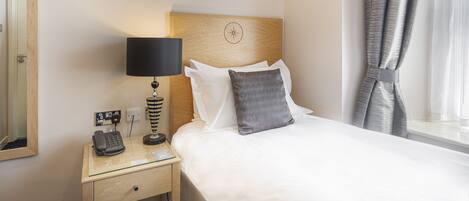 A hotel room with a bed, a bedside lamp, a telephone, and a window with curtains.