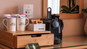 Una estación de café con tazas de marca, una caja de té, un letrero que indica leche fresca y una máquina de café sobre una mesa de vidrio.