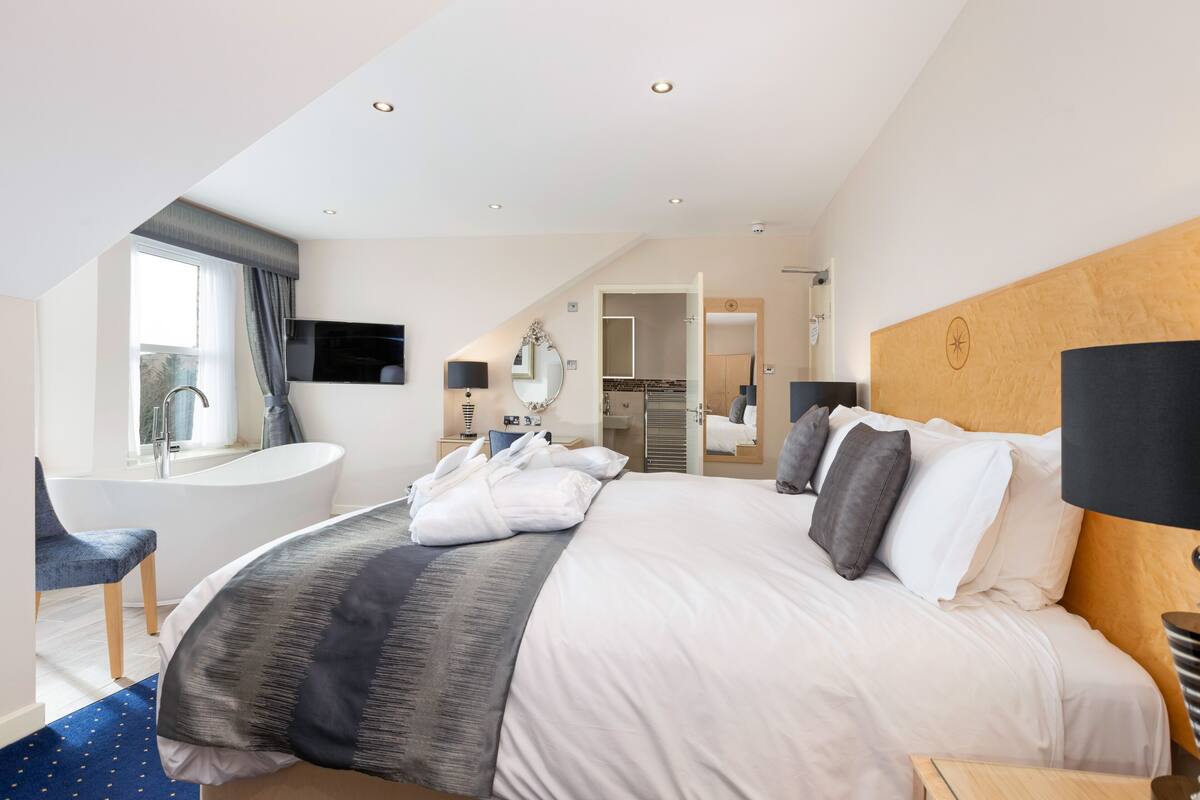 Een moderne hotelkamer met een groot bed, een zithoek met een fauteuil, een badkuip en uitzicht op het omliggende landschap.