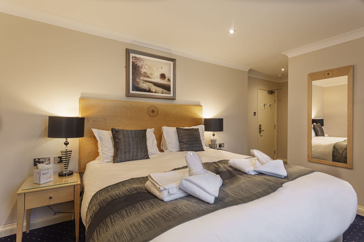 Een hotelkamer met een groot bed, twee nachtkastjes, een spiegel aan de muur en een lijst met een afbeelding boven het bed.