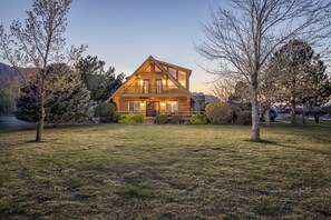 Une cabane en rondins dotée d’un porche à l’avant, d’un balcon et d’une pelouse bien entretenue.