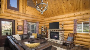 Ein Blockhaus-Interieur mit Kamin aus Stein, einer Ledersofa und einem darüber montierten Fernseher.