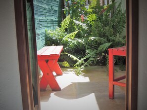 A red table and bench in a garden area with lush greenery and a concrete floor. - Nossa Casa em Jeri (Jijoca de Jericoacoara)