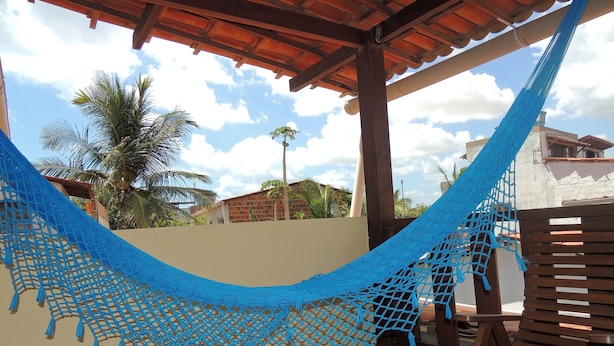 A hammock under a wooden pergola with a view of a residential area and palm trees. - Nossa Casa em Jeri (Jijoca de Jericoacoara)