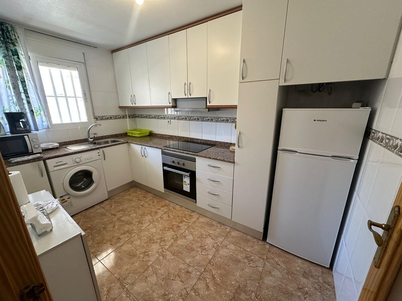 Una cocina compacta con armarios blancos, lavadora, horno, microondas y refrigerador.