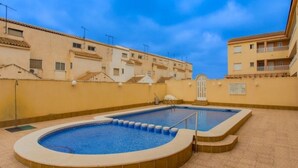 Una piscina sul tetto con due aree distinte, circondata da edifici beige con balconi, sotto un cielo sereno.