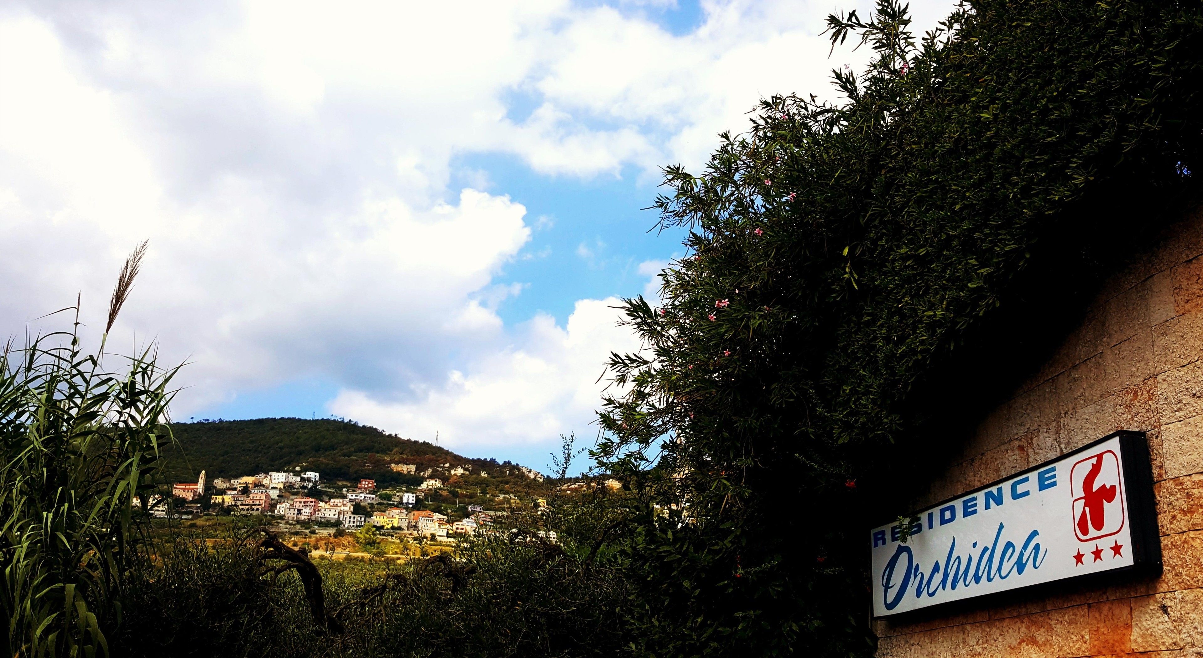Un panneau indiquant une résidence à Orkidea, avec vue sur un village perché sur une colline.