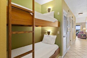 Dormitorio con literas de madera, una lámpara fijada a la pared y una puerta que da a otra habitación.