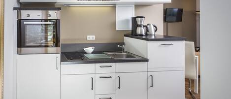 Una cocina compacta con horno integrado, cafetera y microondas.