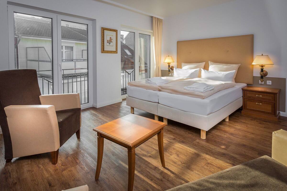 A hotel room with a bed, bedside tables, a chair, a small table, and a view through a glass door.