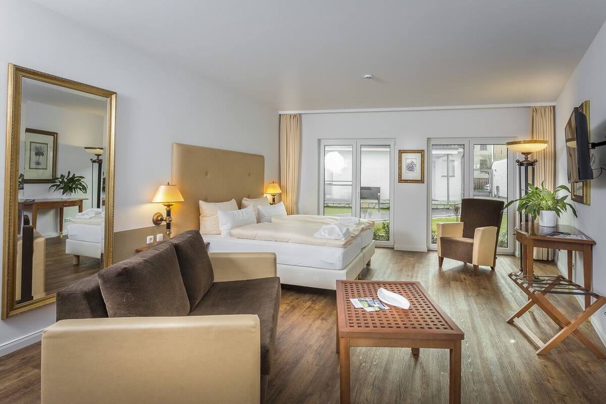 A hotel room with a bed, a sofa, a table, a TV, and a large window.