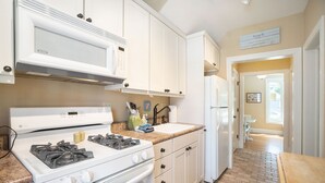 A kitchen with white cabinets, a stove, a microwave, and a sink.