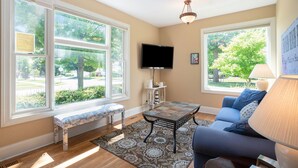 A living room with large windows, a bench, a sofa, a table, and a TV.