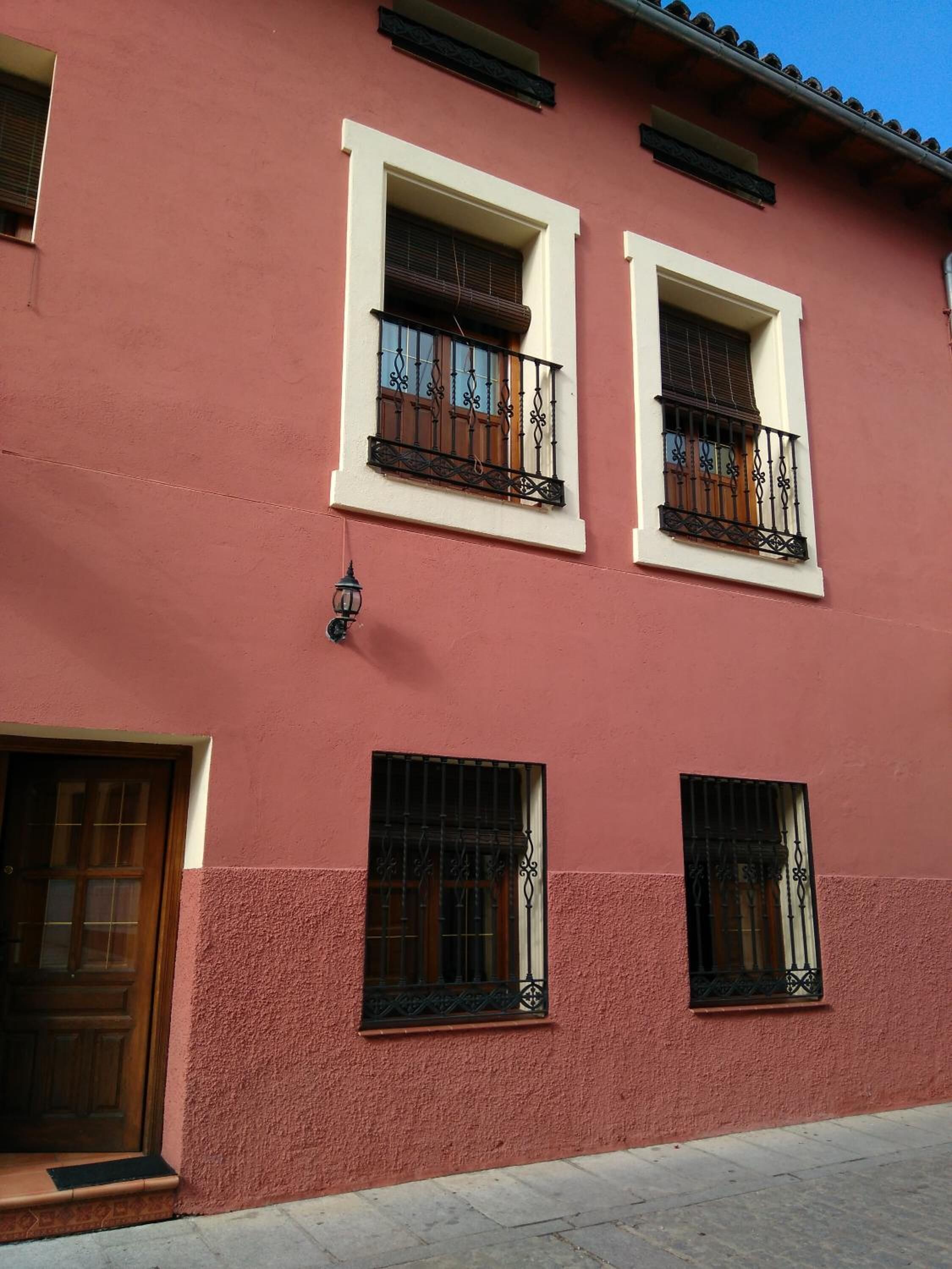 Un edificio con tres ventanas, cada una con un balcón y una pequeña lámpara fijada a la pared.