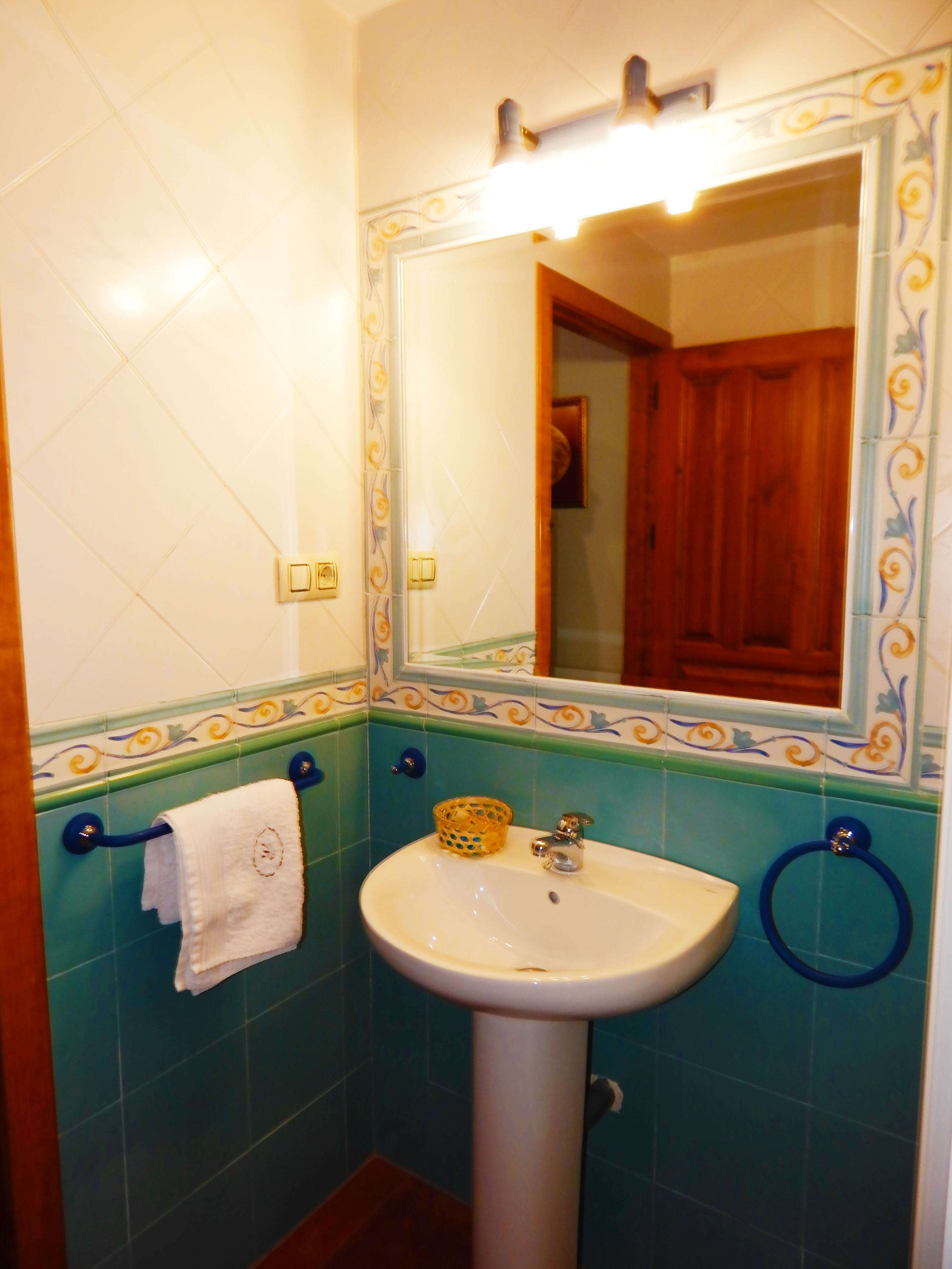 Un baño con un lavamanos blanco, aros para toallas azules y un espejo con detalles de azulejos decorativos.