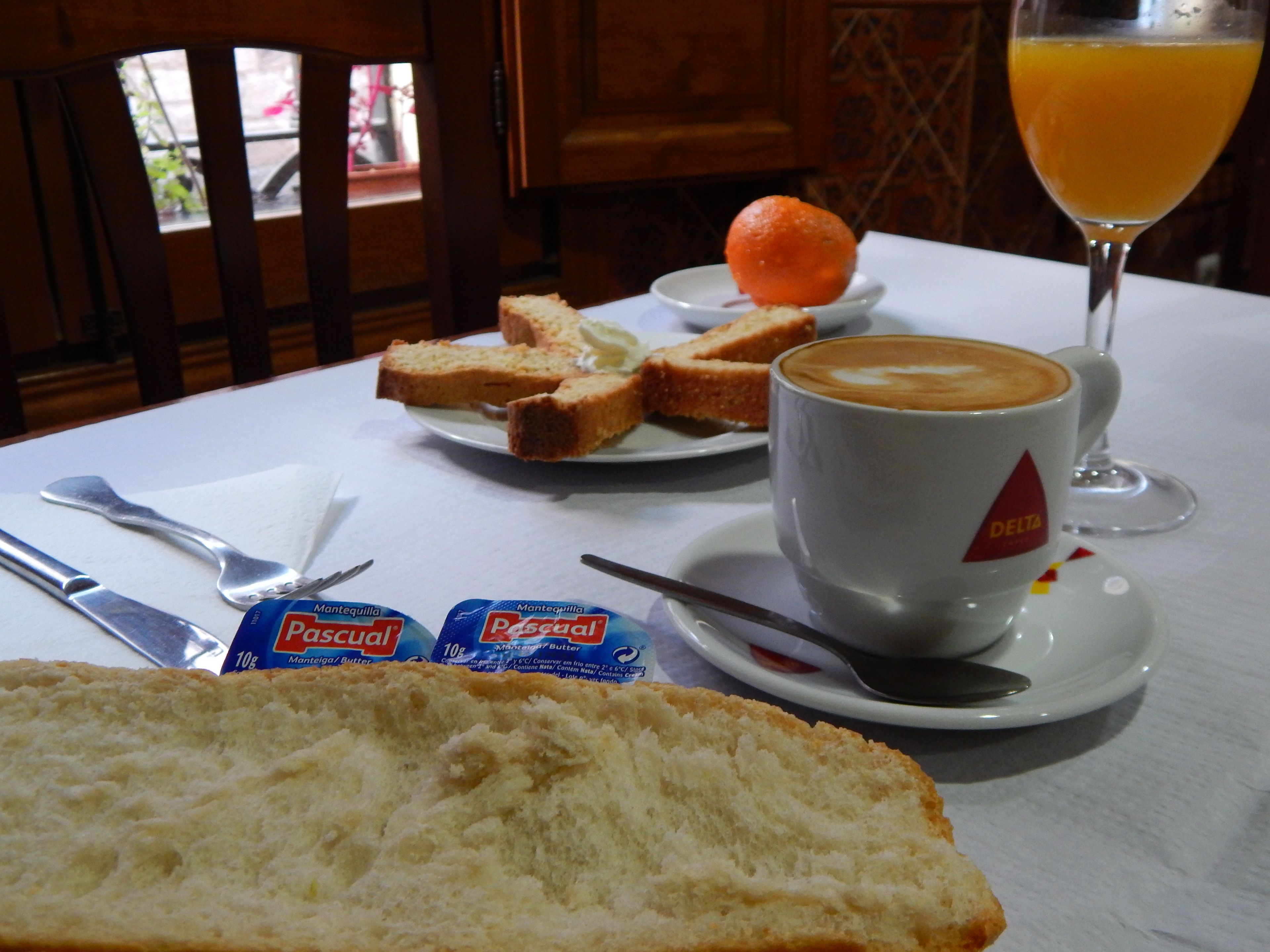 A breakfast table with bread, butter, orange, and a glass of orange juice.