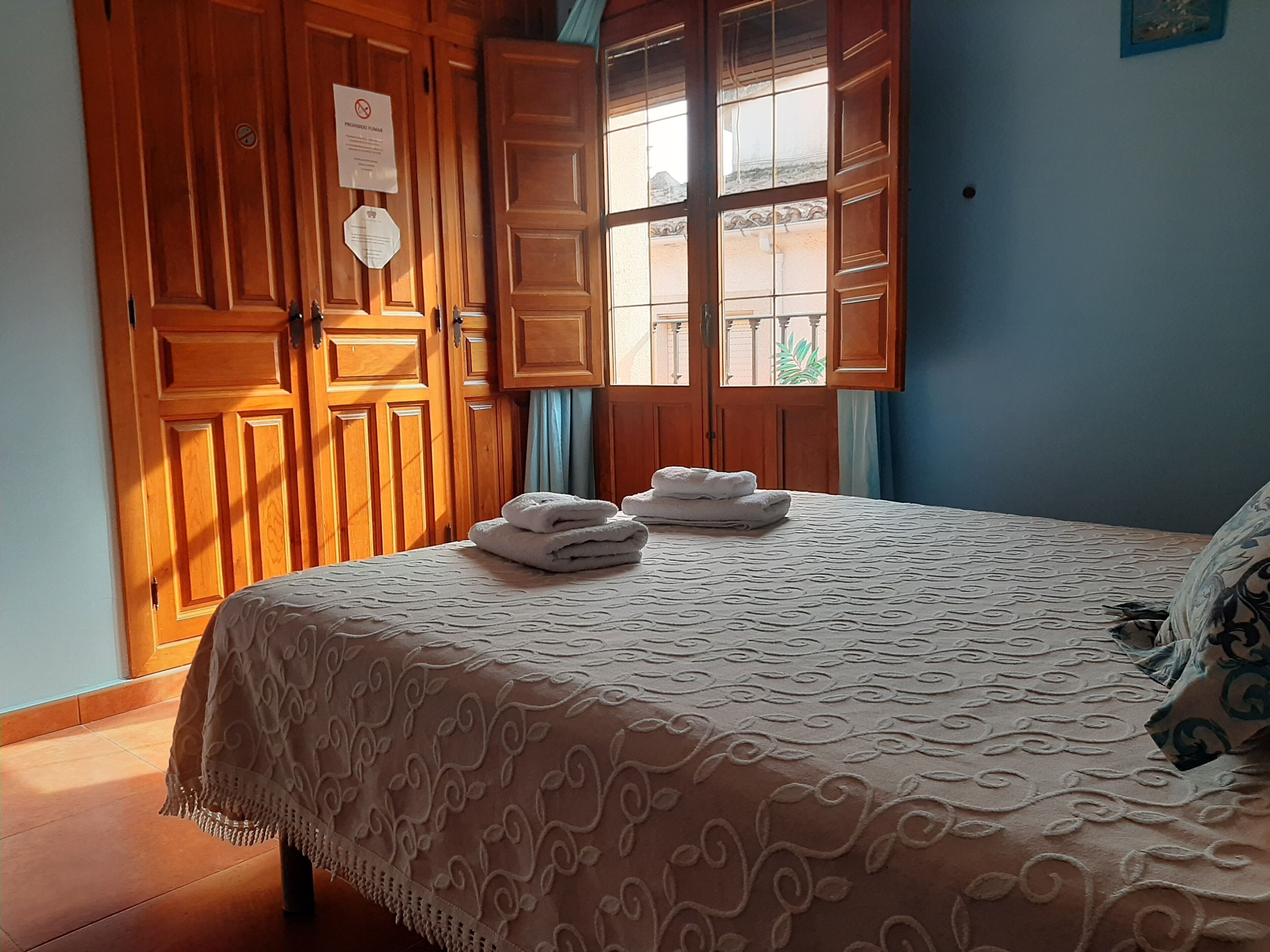 A room with a bed, wooden wardrobe, and a window with curtains.