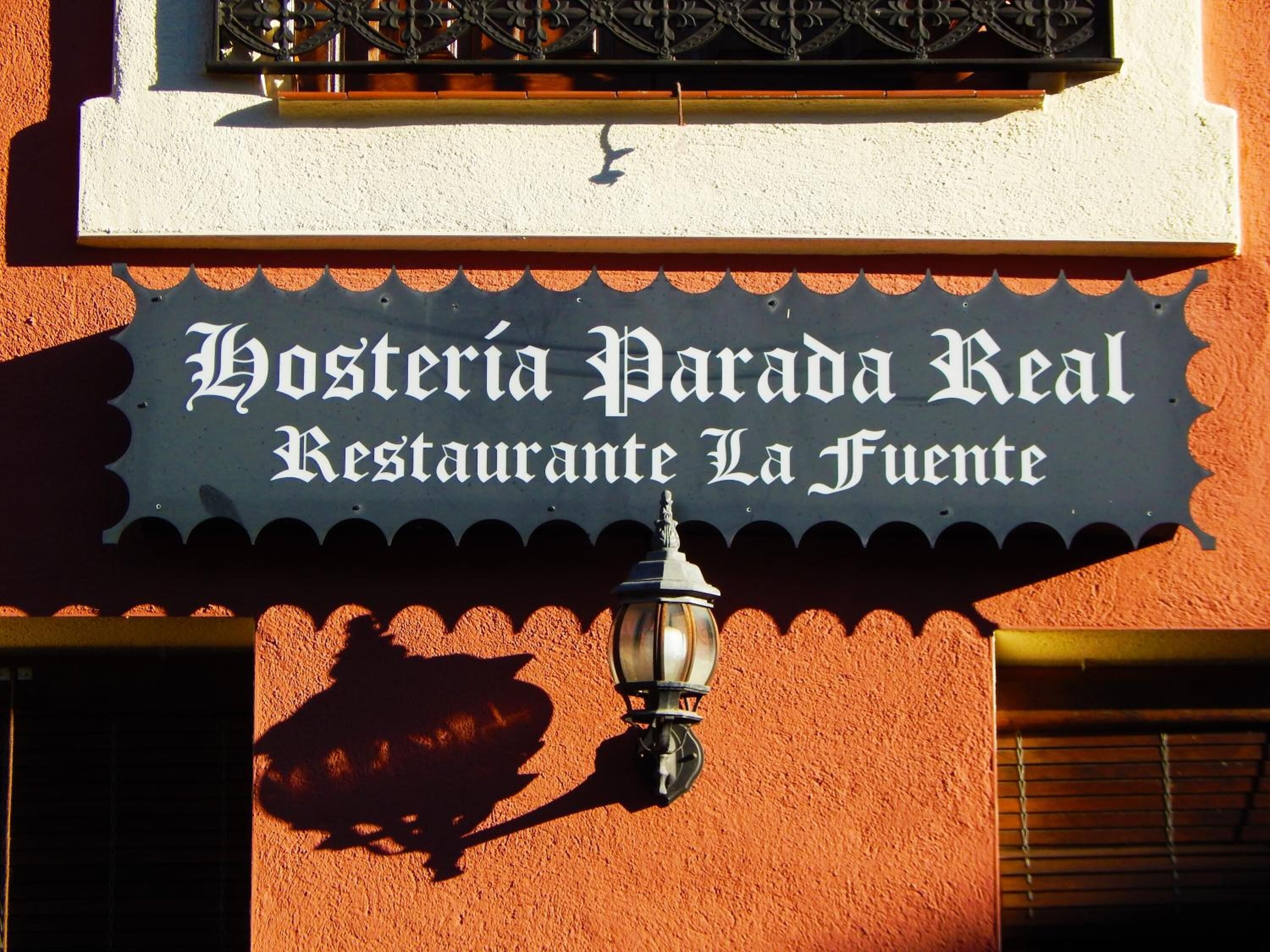 En restaurangskylt med namnet ”Hostería Parada Real Restaurante La Fuente” på en vägg med en tydlig struktur.