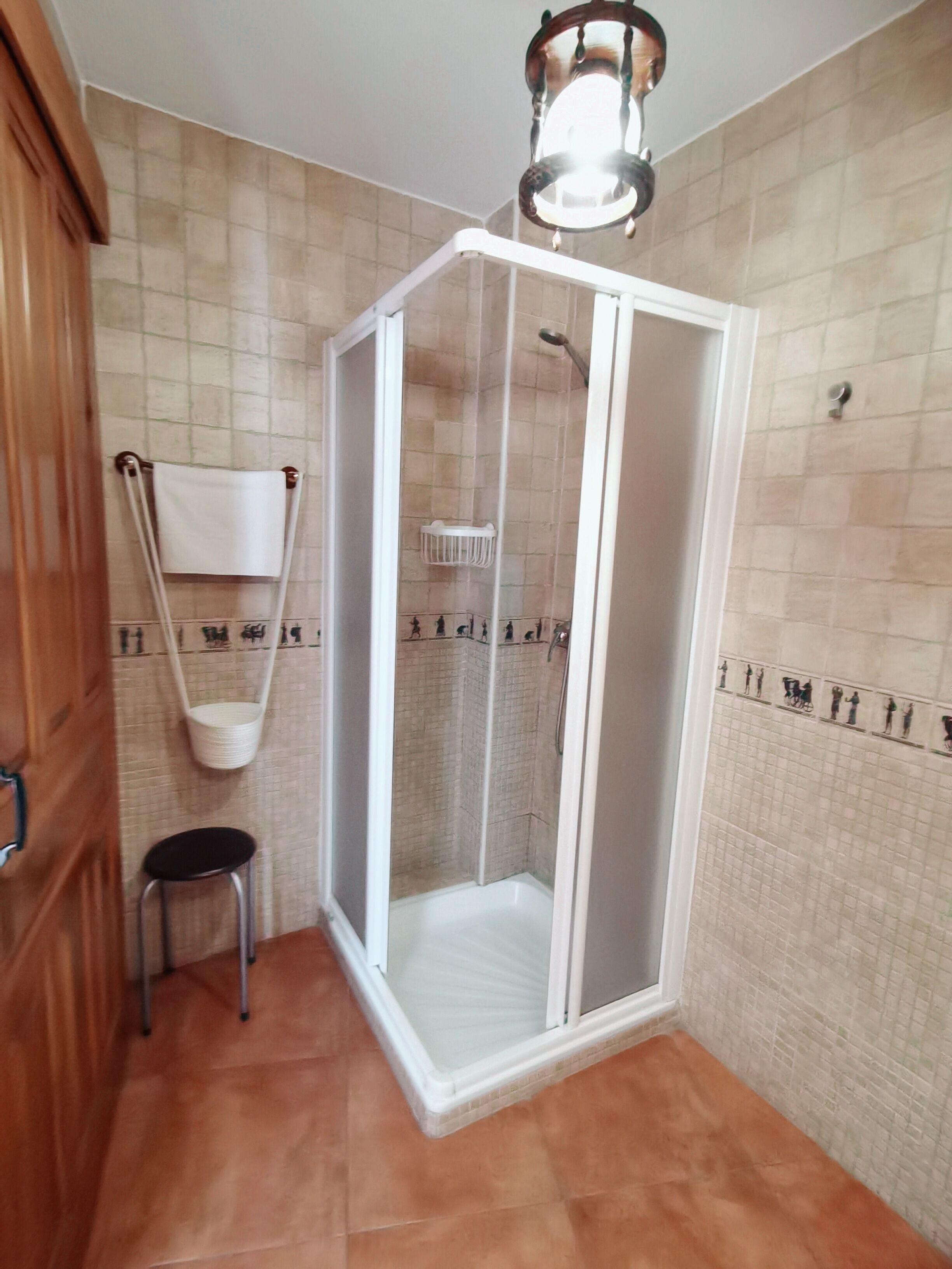 Un espace douche doté d’une porte en verre, d’un porte-serviettes mural et d’un petit tabouret.