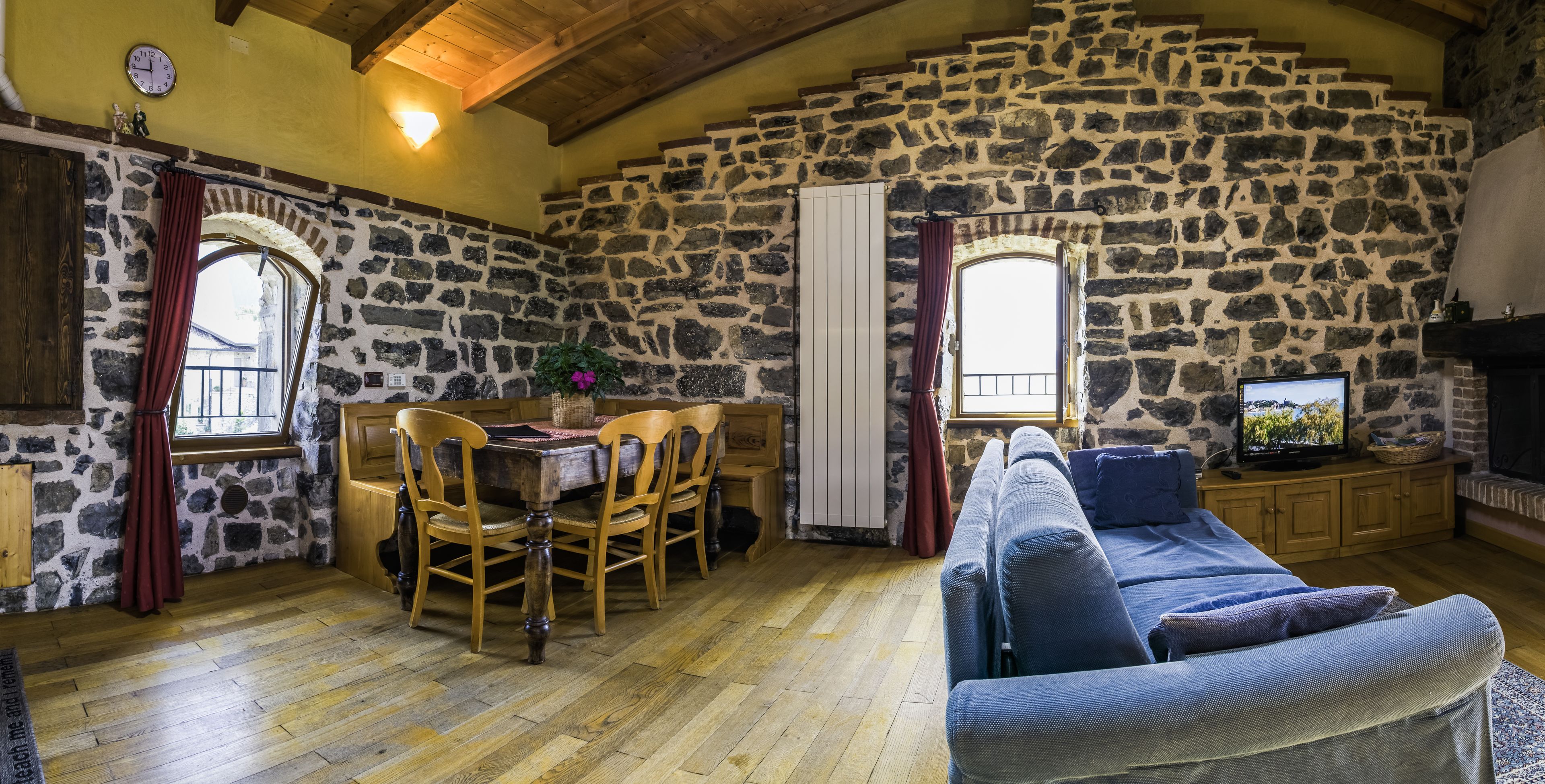 Een rustiek interieur met stenen muren, een houten eettafel met stoelen, een bank en een televisietoestel.
